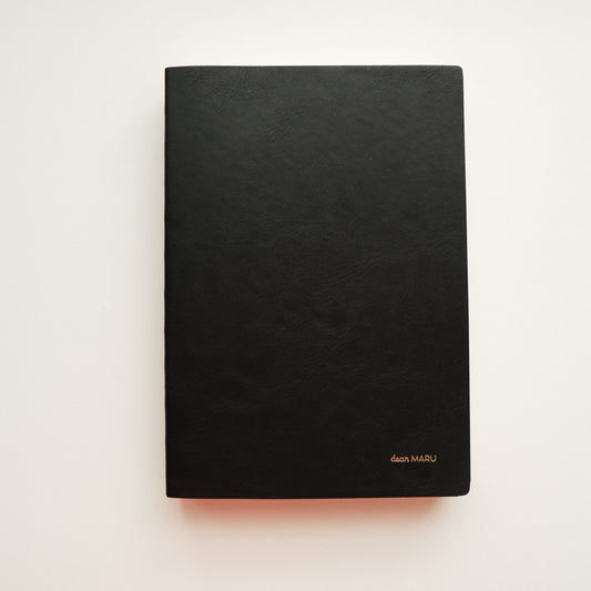 A notebook with a soft, buttery-textured black leatherette cover with a small gold foil logo reading "Dear MARU" in the bottom right corner, photographed flat on a clean white background. 